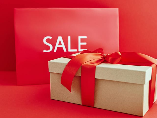 cardboard box with red ribbon beside a sale sign